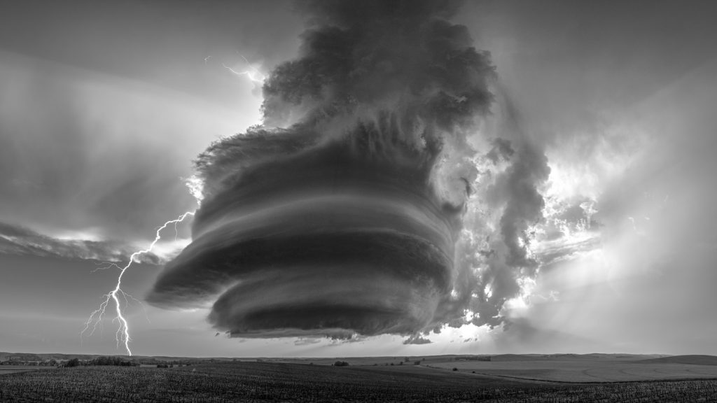 A black-and-white photo shows swirling winds and a bolt of lightning striking over open fields.