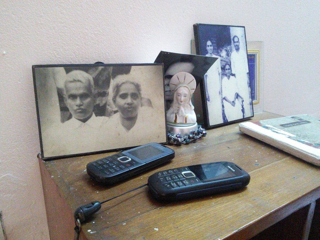 Two cellular phones sit on a small wooden shelf beside family photos and other mementos.